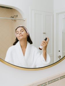 woman in mirror, spraying face 