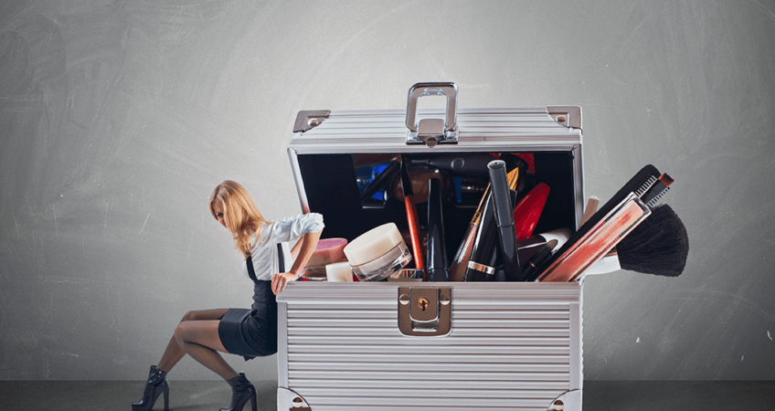 The image features a woman sitting beside a large, overflowing makeup organizer. The silver case, packed with cosmetics like lipsticks, mascara, and brushes, creates a playful and exaggerated scene, emphasizing the need for organization in beauty routines.